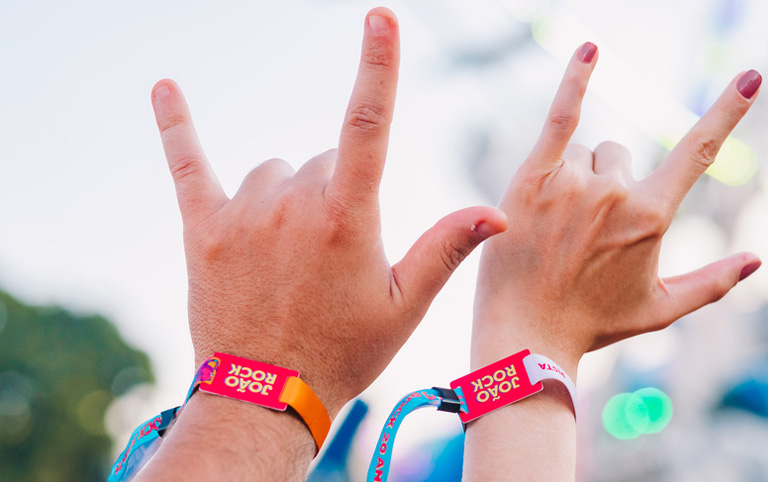 Fotografia colorida de mãos com pulseira de acesso do João Rock - Divulgação